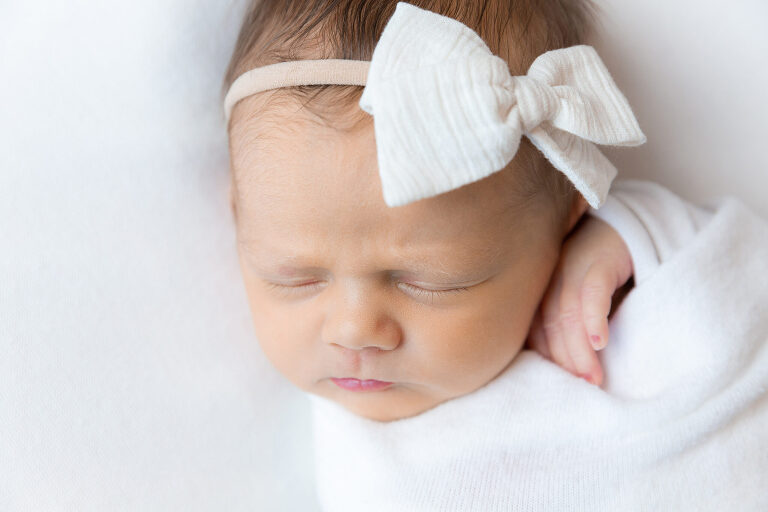 Newborn baby with white bow on her head during her newborn photography session in Huntsville, Alabama